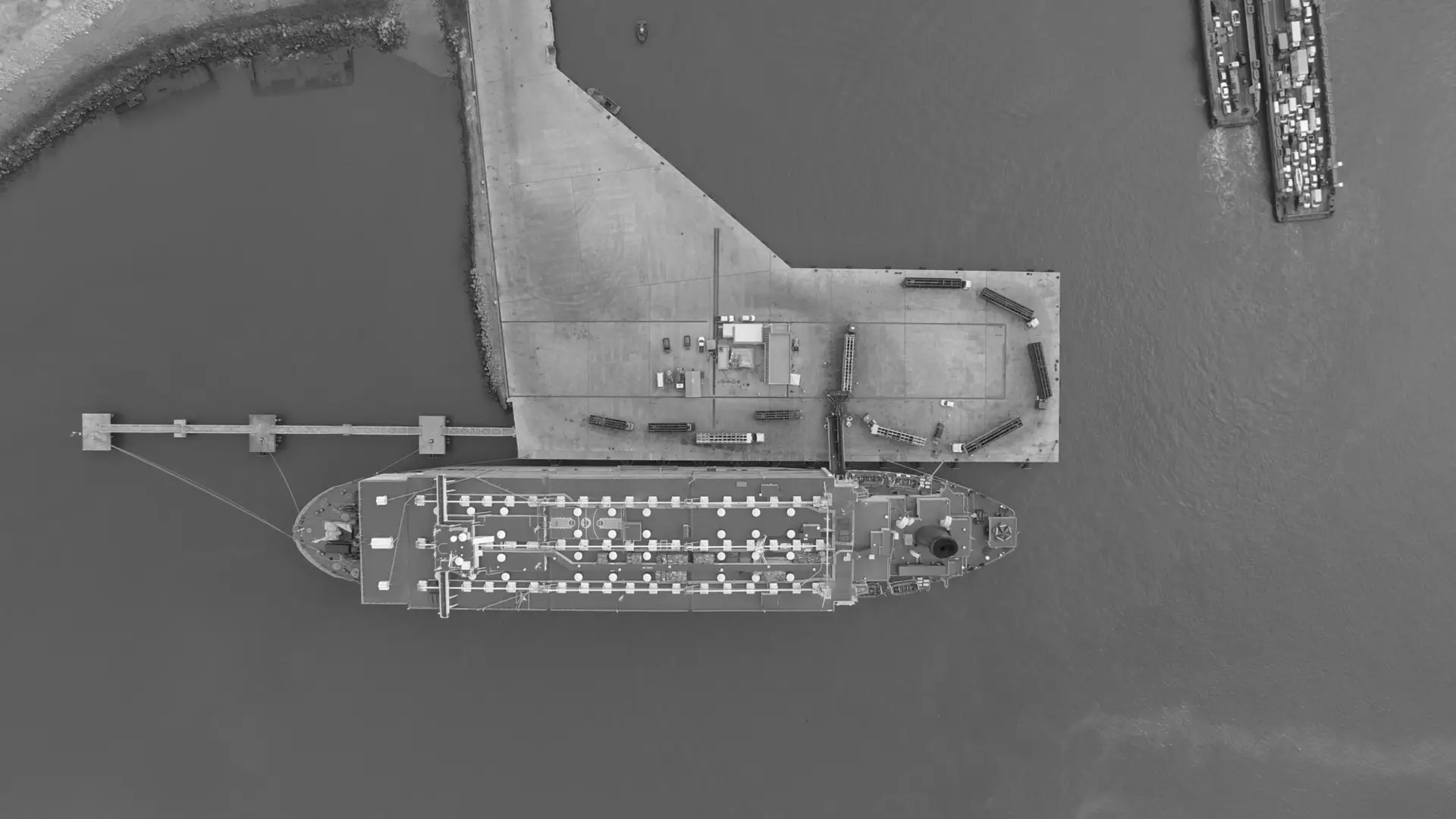 Aerial view of a cargo ship docked at a port terminal, freight staged on the pier